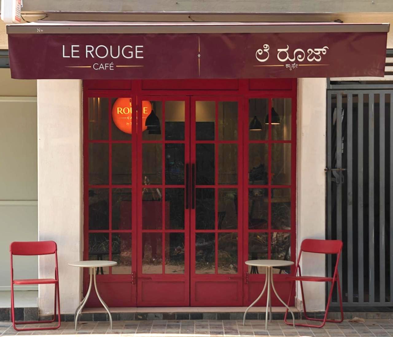 The Le Rouge Café storefront on Byrathi Bande, with red framed doors and pavement seating
